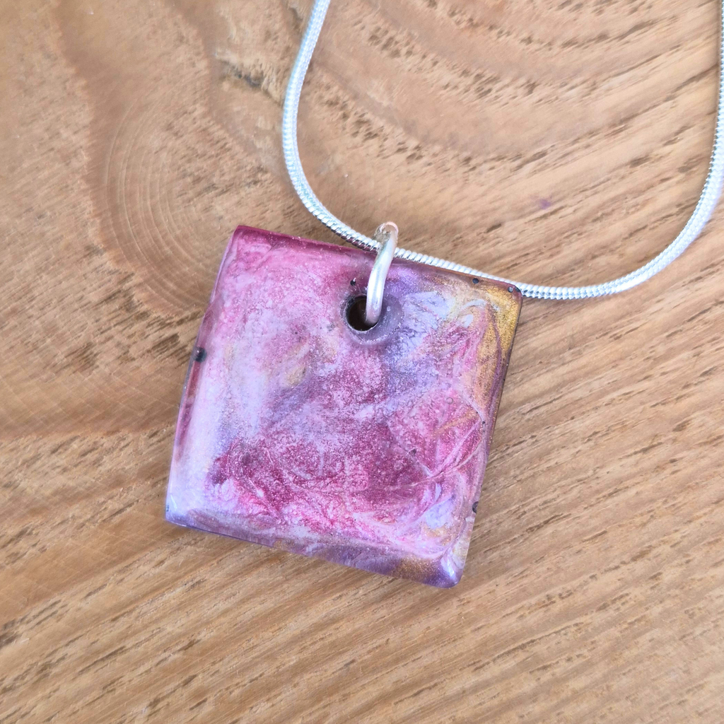 Square pink and purple pendant on a chain against a wooden background