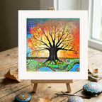 Colourful tree of life painting on a wooden easel with decorative stones on a wooden surface.
