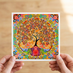 Colourful tree of life artwork held by hands on a wooden surface