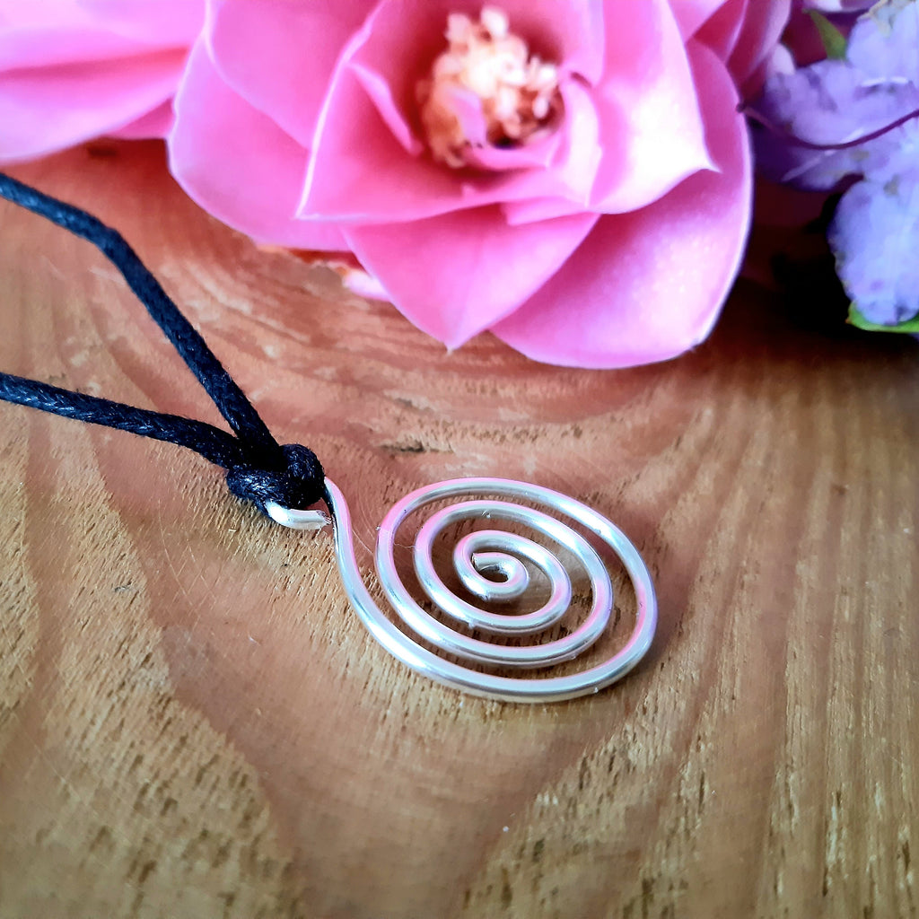 Spiral pendant on a string with pink flowers in the background