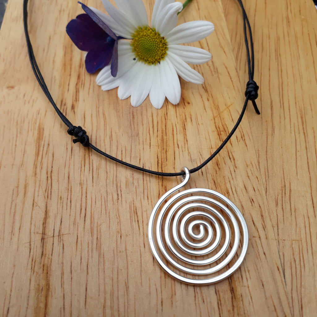 Silver spiral pendant on a black cord with a daisy on a wooden surface