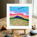 Colourful abstract landscape painting on a wooden easel with natural elements.