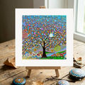 Colourful abstract tree of Life painting on a wooden easel with decorative stones on a wooden surface.