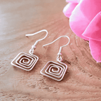 Pair of spiral design earrings on a wooden surface with pink fabric in the background