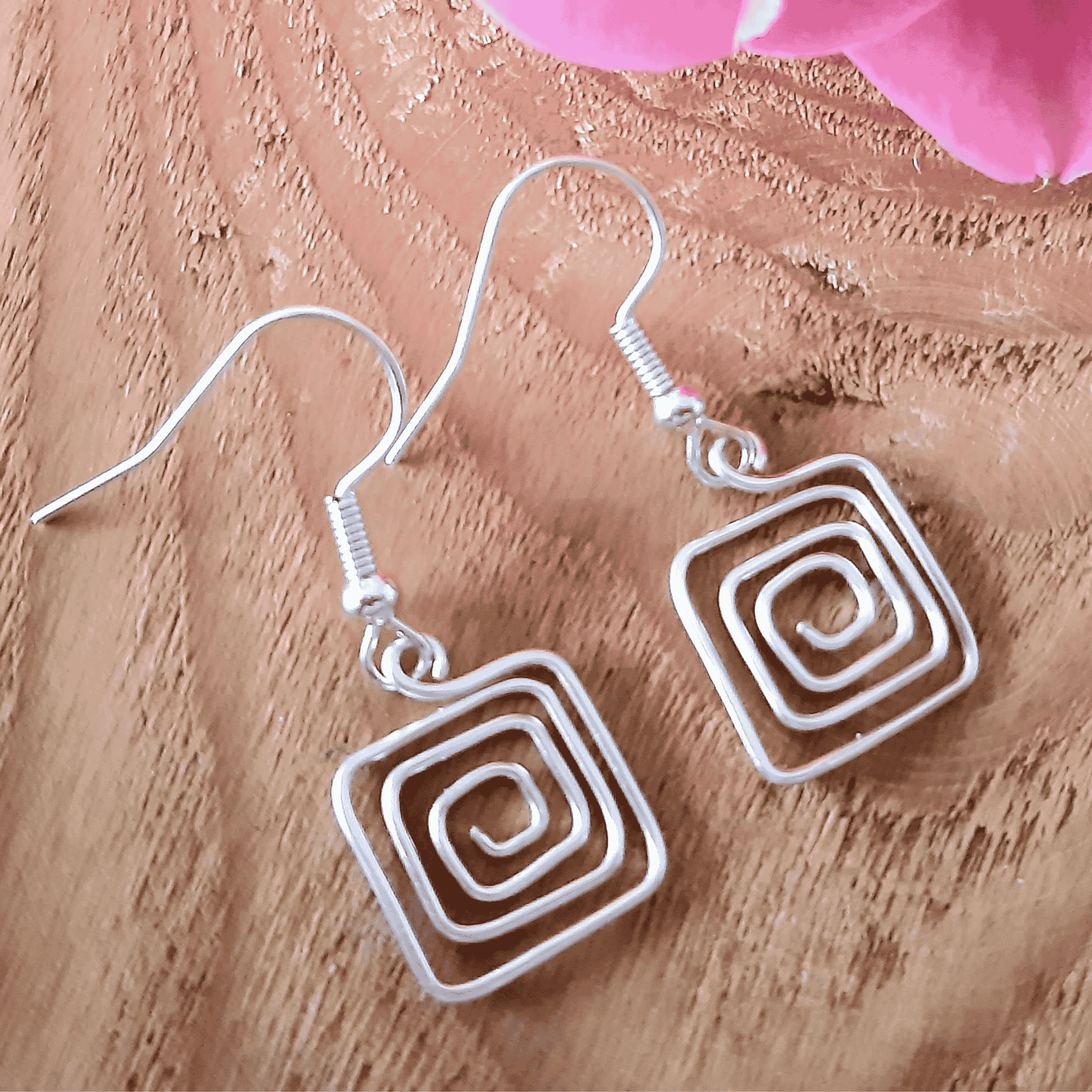 Silver spiral earrings on a textured brown surface with pink flowers.