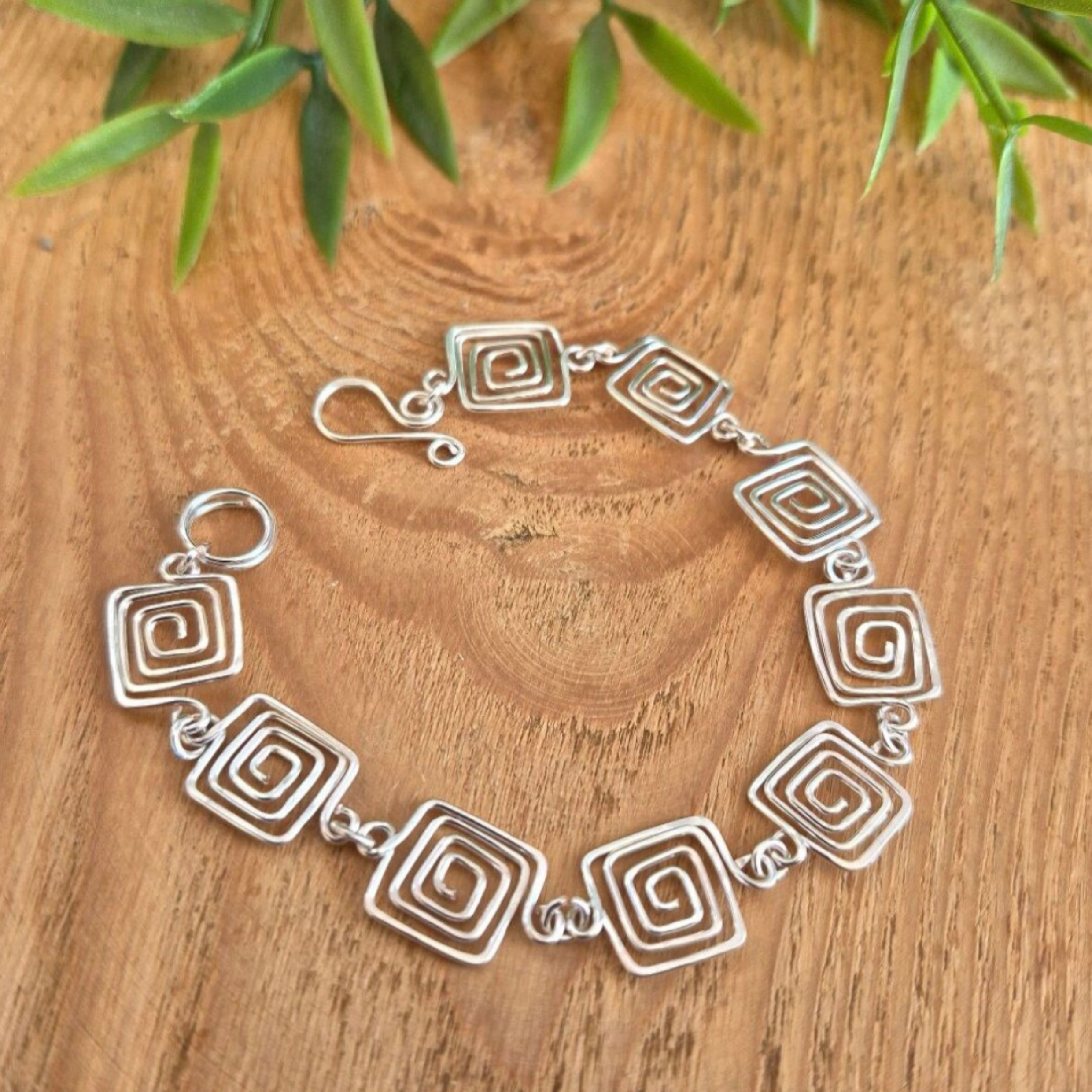 Silver bracelet with spiral designs on a wooden surface with green leaves.