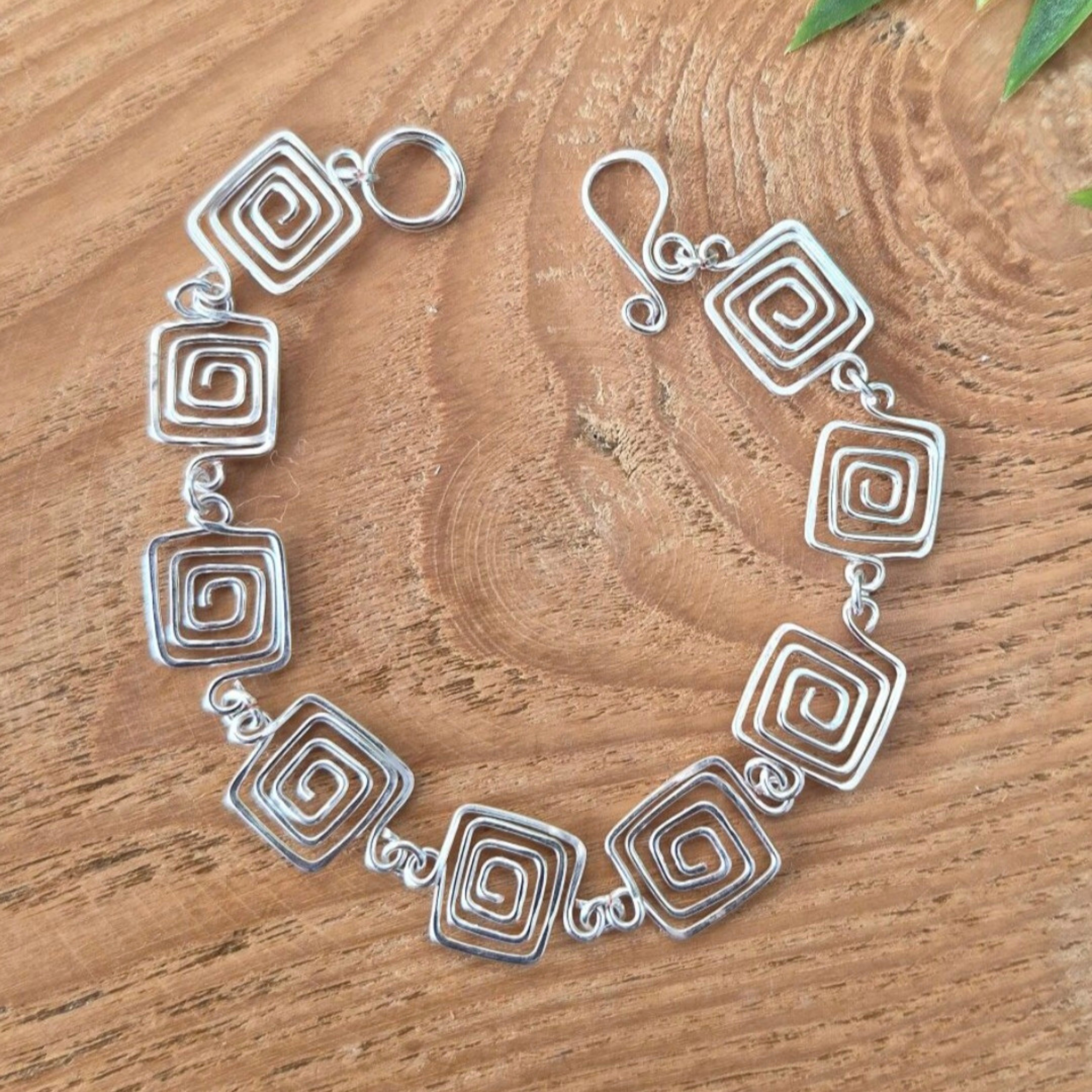 Silver bracelet with spiral designs on a wooden surface