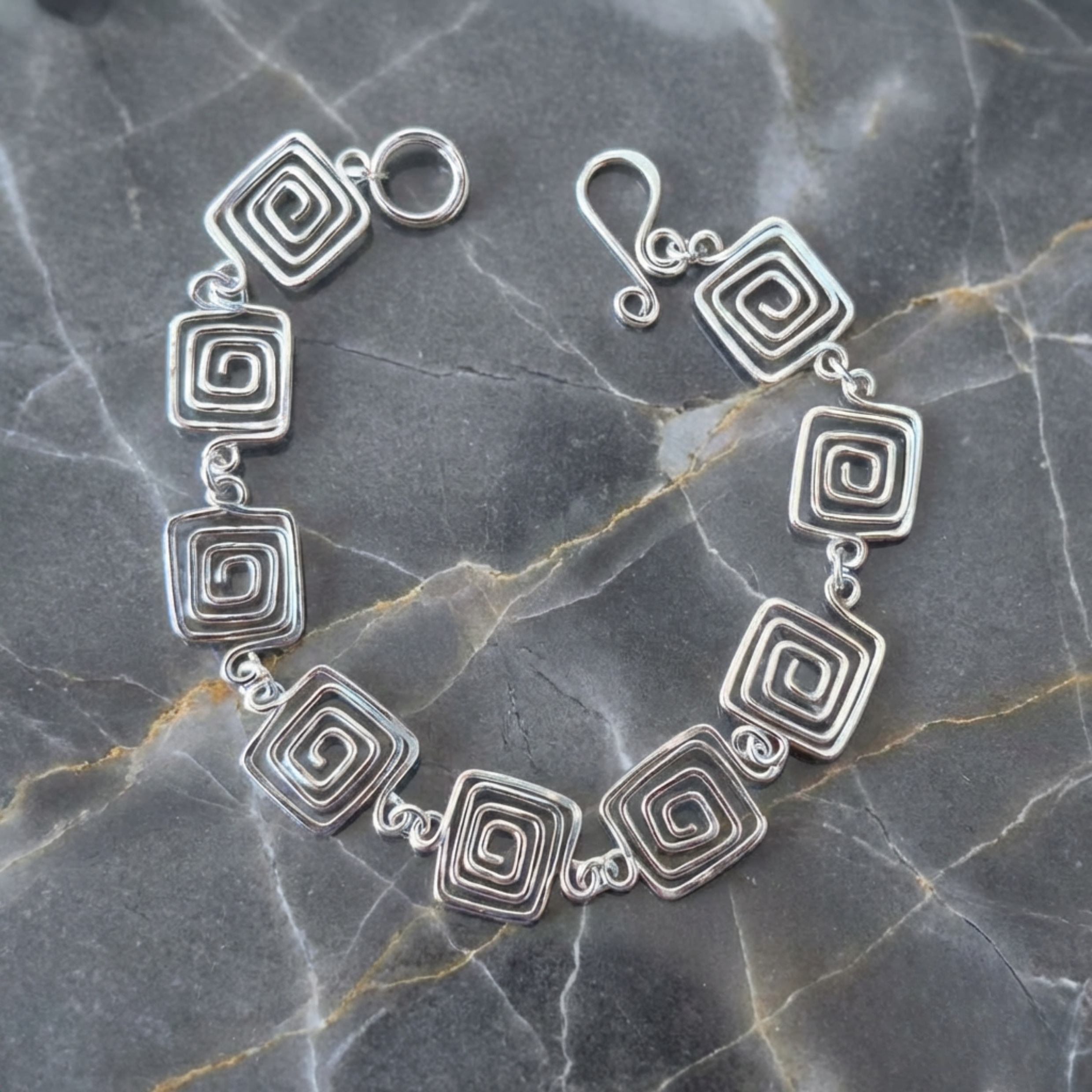 Silver bracelet with spiral designs on a gray marble surface