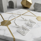 Silver square earrings on a marble surface with geometric background