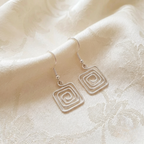 Silver square spiral earrings on a beige fabric background
