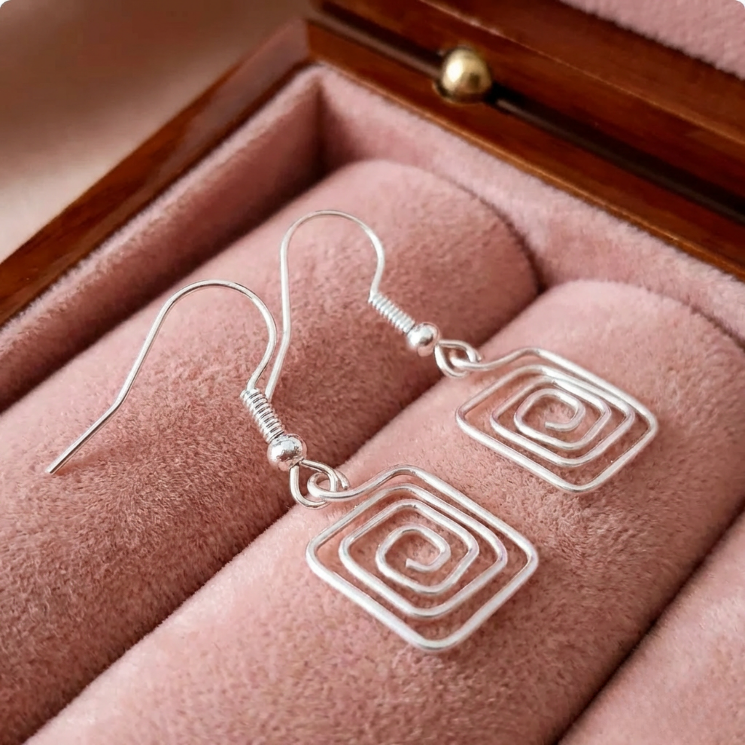 Silver spiral square earrings on a pink cushion in a jewellery box