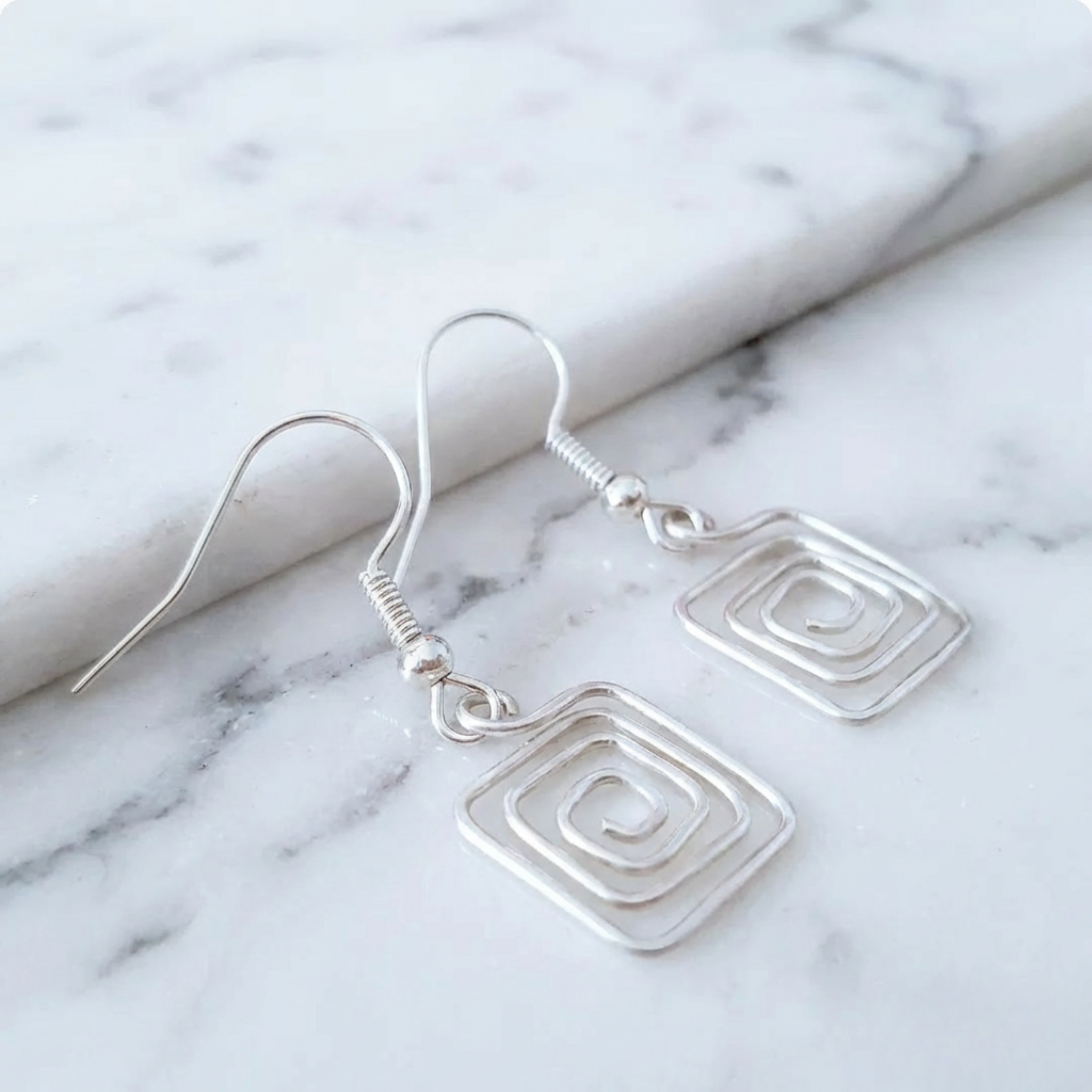 Silver square earrings on a marble surface