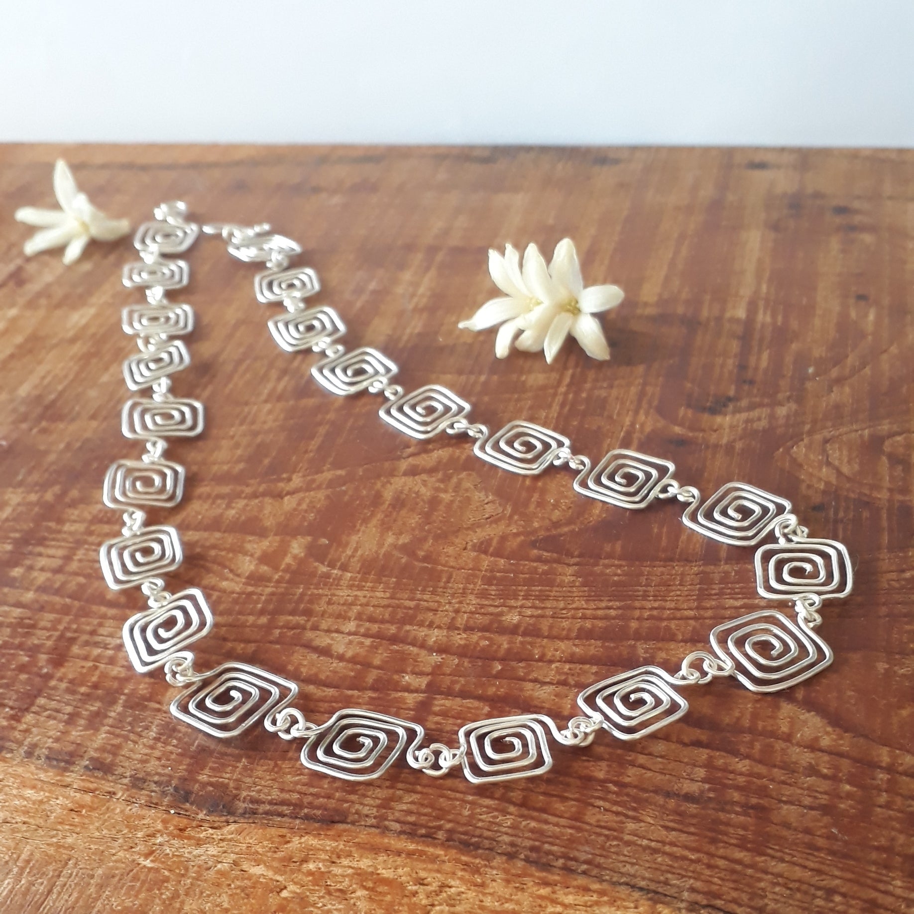 Silver necklace on a wooden surface with white flowers