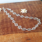 Silver necklace on a wooden surface with white flowers