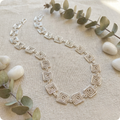 Silver necklace with geometric design on a textured surface with eucalyptus leaves and stones.