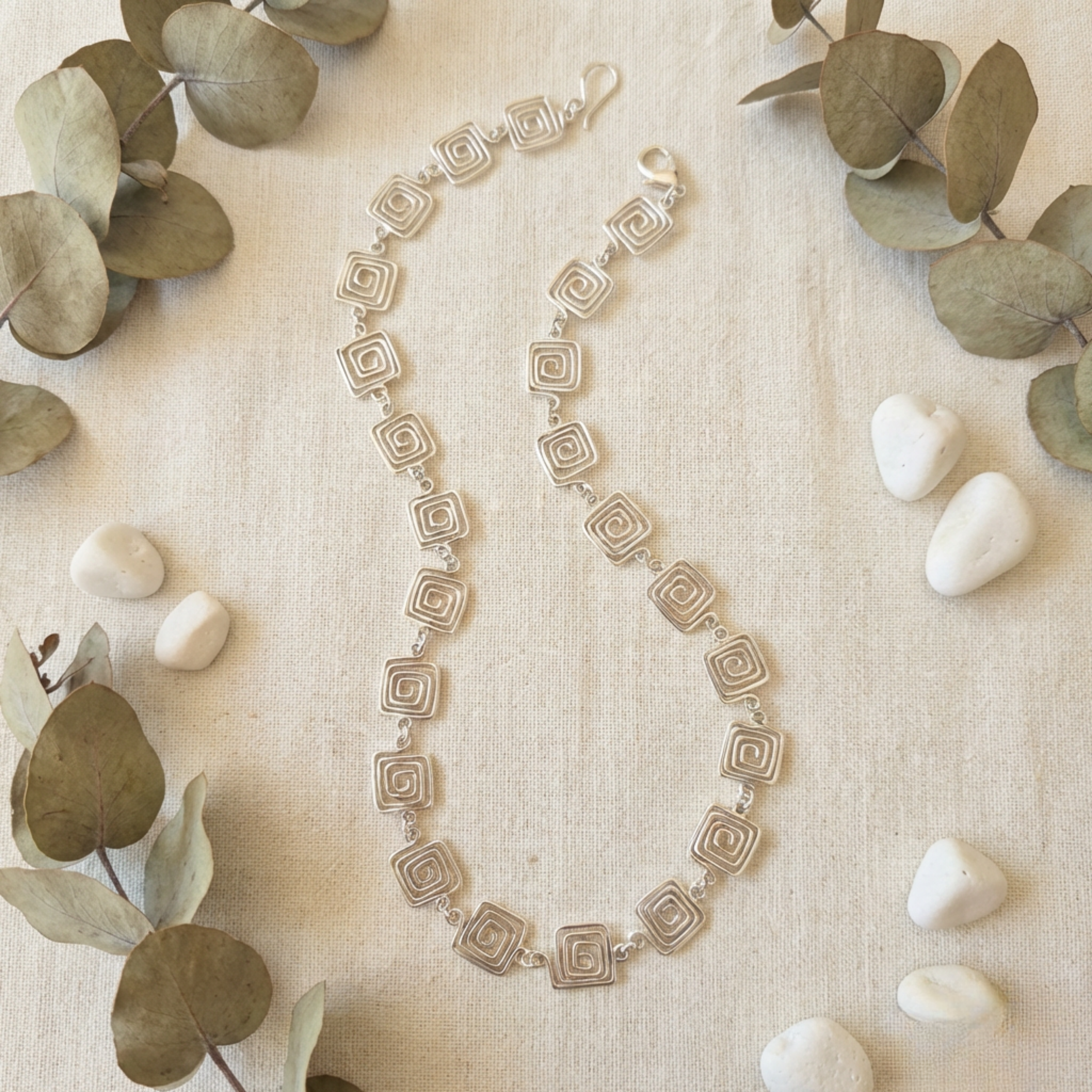 Silver square spiral necklace on a fabric backgrond with foliage