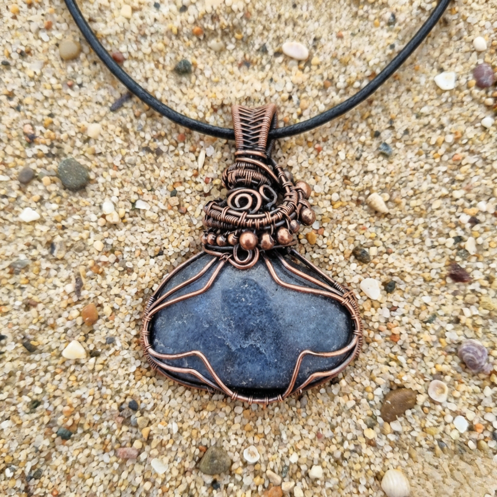 Necklace with a blue stone pendant on a sandy background