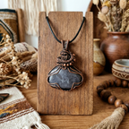 Necklace with a large pendant on a wooden stand, surrounded by decorative items.