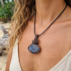 Person wearing a necklace with a blue pendant on a beach