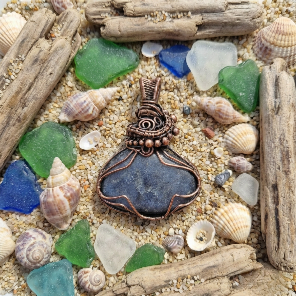 Pendant with blue stone and copper wirework on a sandy background with shells and driftwood