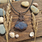 Copper pendant with blue stone on a wooden surface with stones and shells