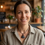 Woman smiling in a cozy indoor setting with wooden furniture and plants.