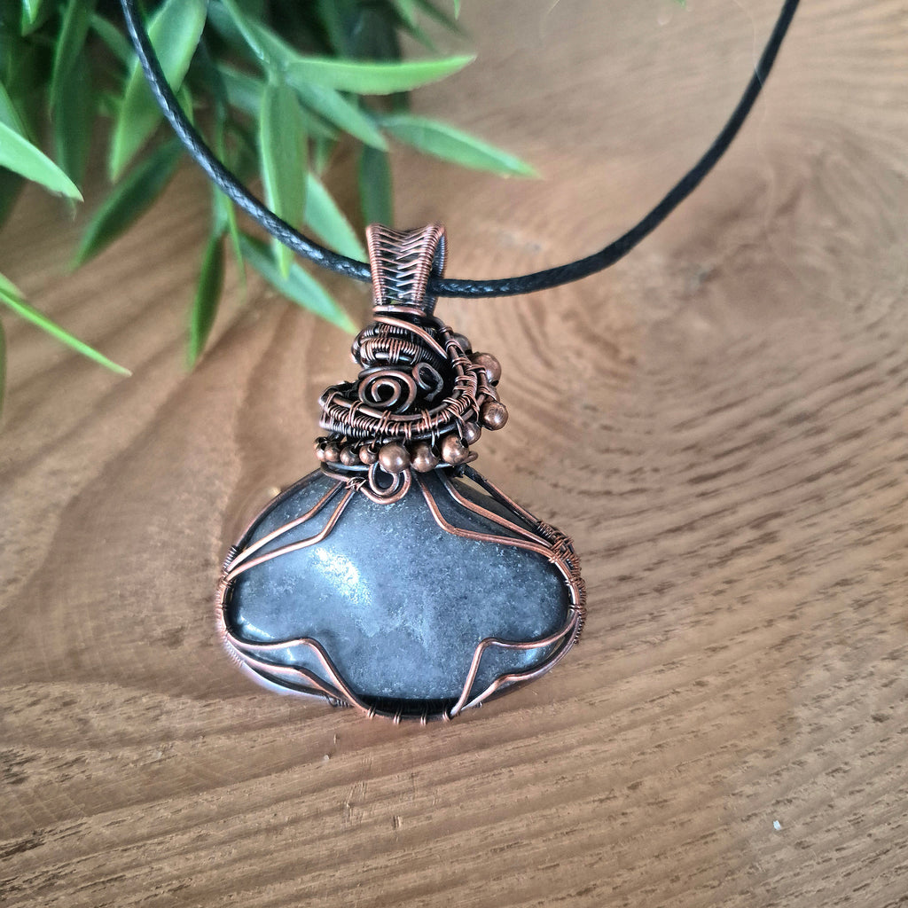 Decorative pendant necklace on a wooden surface with greenery in the background