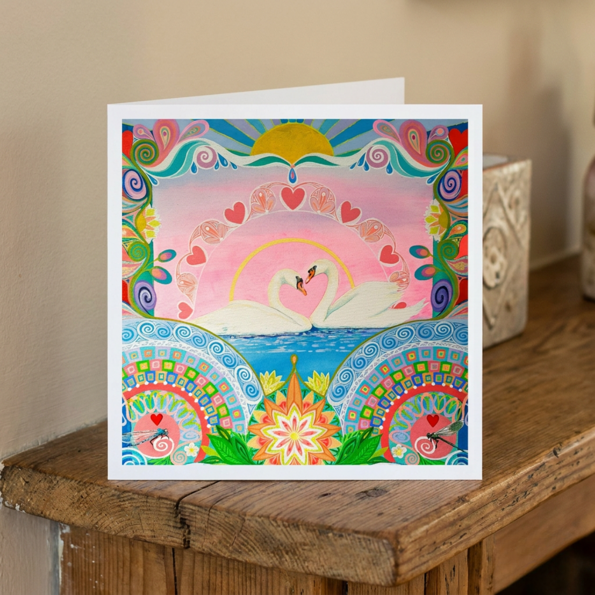 Colourful greeting card with swans and decorative patterns on a wooden surface.