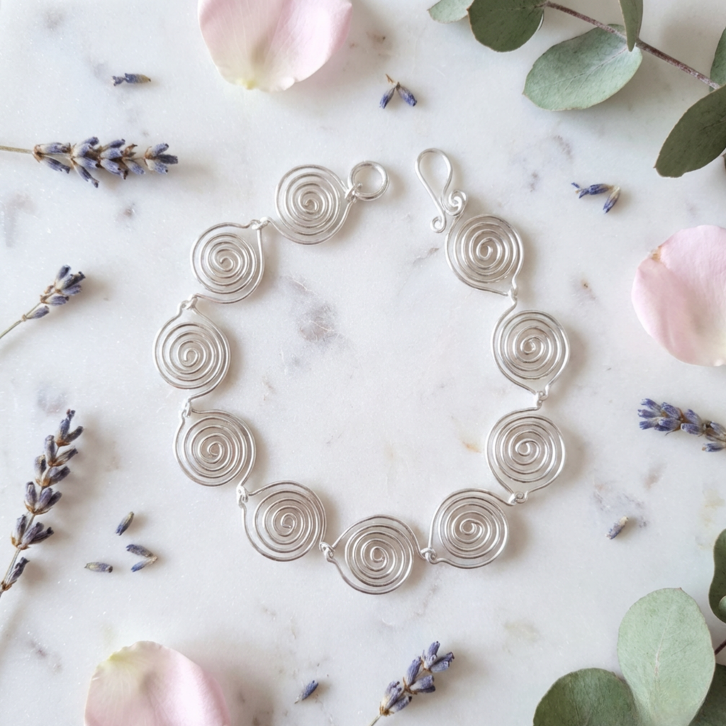 Silver spiral bracelet on a marble surface with flowers and lavender.