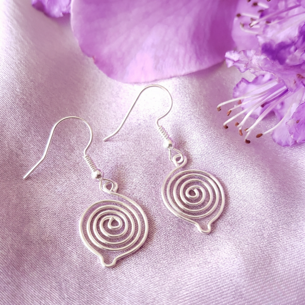 Silver spiral earrings on a pink fabric background with purple flowers.