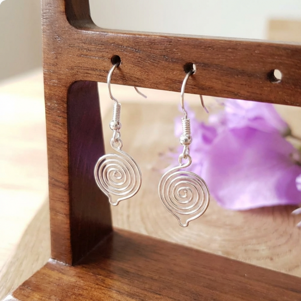 Silver spiral earrings on a wooden stand with a blurred purple flower in the background