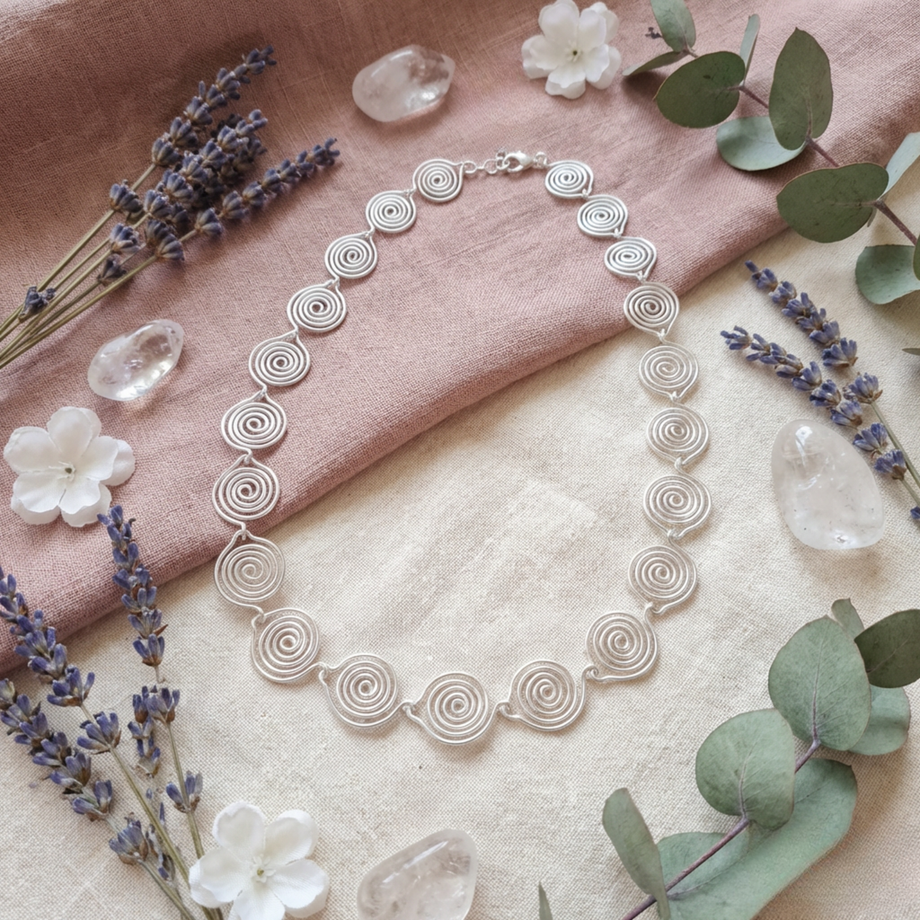 Silver necklace with floral and lavender decorations on a soft pink fabric background