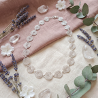 Silver necklace with floral and lavender decorations on a soft pink fabric background