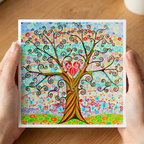 Colourful tree of life artwork held by hands on a wooden surface