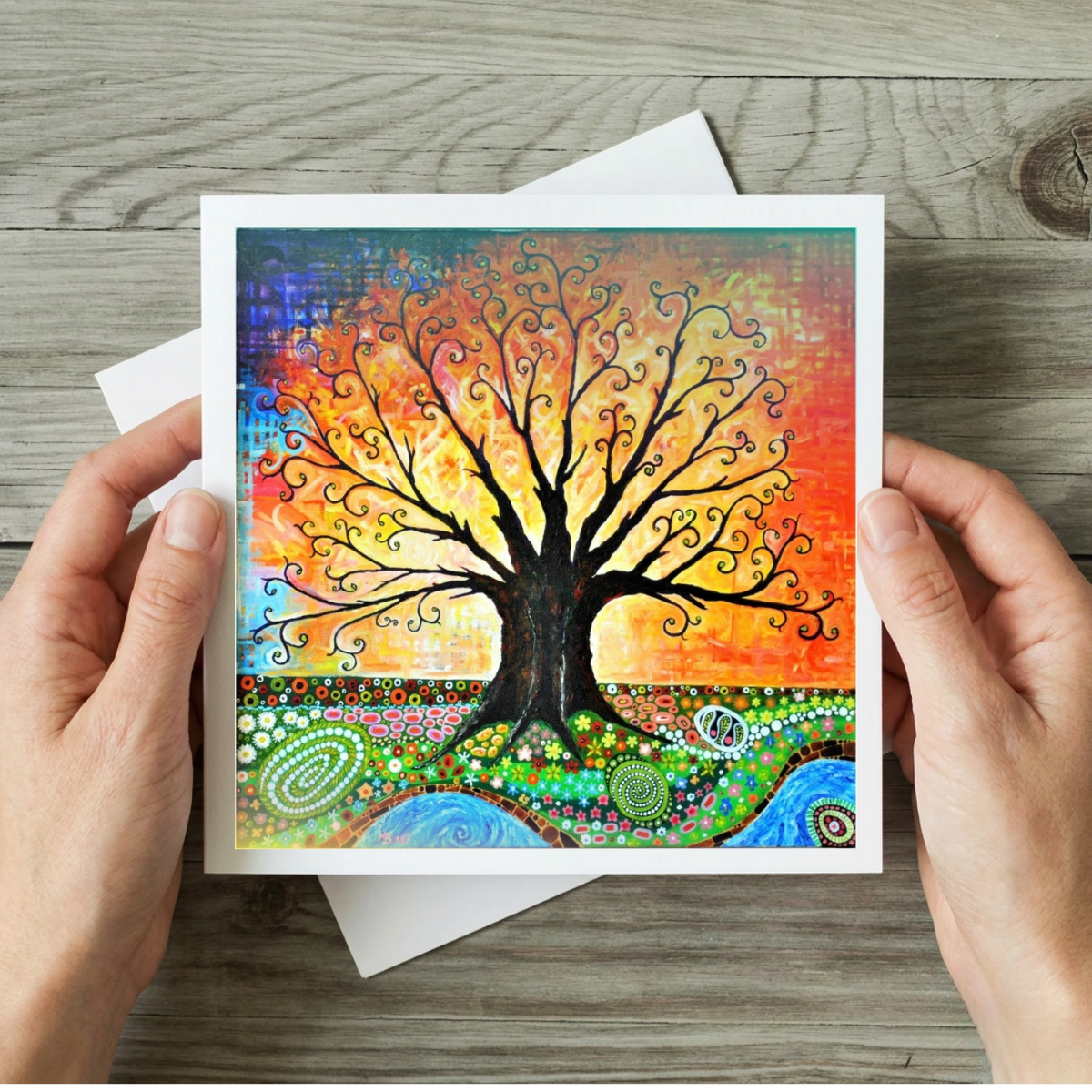Colourful tree of life artwork held by hands on a wooden surface