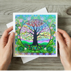 Colourful tree of life card held by hands on a wooden surface