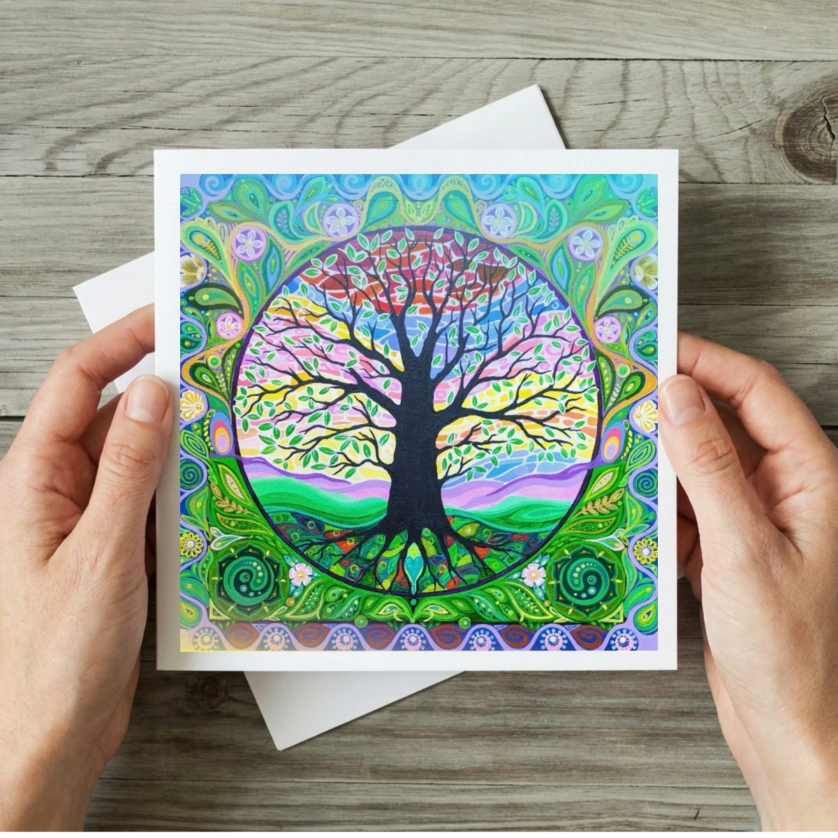 Colourful tree of life card held by hands on a wooden surface