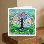 Colourful tree of life design on a greeting card with a white envelope, placed on a wooden surface.