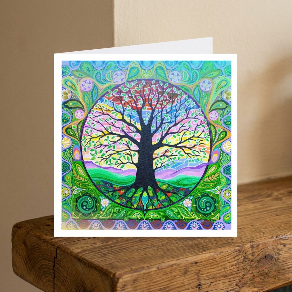 Colourful tree of life design on a greeting card with a white envelope, placed on a wooden surface.