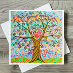 Colourful tree of life with a heart design on a card with a white envelope on a wooden surface