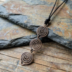 Bronzed copper spiral pendant necklace on a stone surface