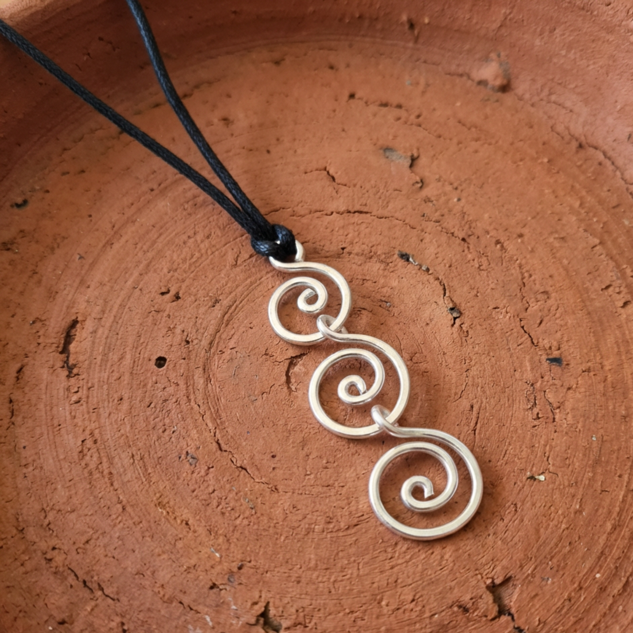 Silver spiral pendant on a black cord against a brown textured background