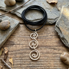 Black leather cord necklace with a decorative pendant on a wooden surface with stones and leaves.