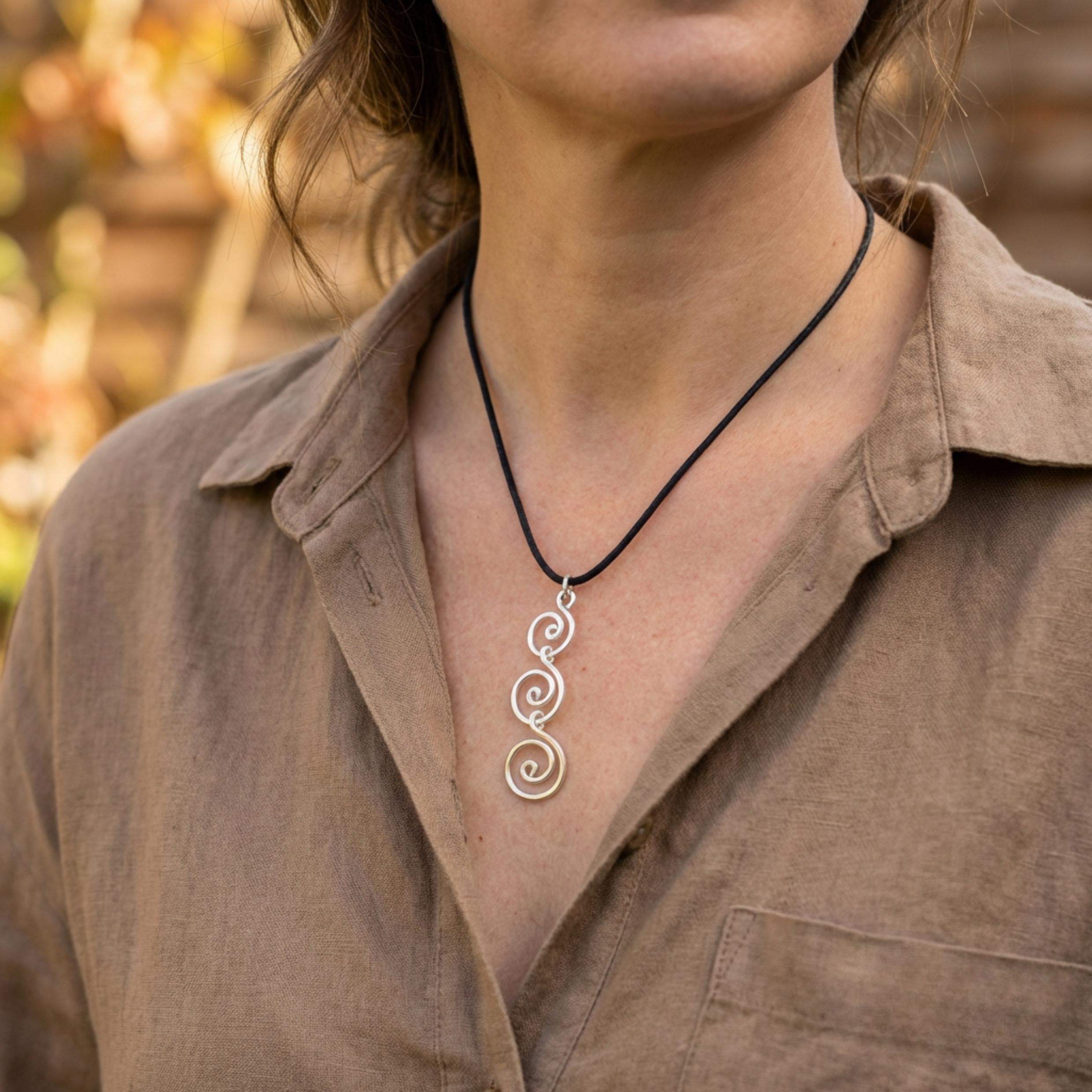 Person wearing a silver spiral pendant necklace with a blurred outdoor background