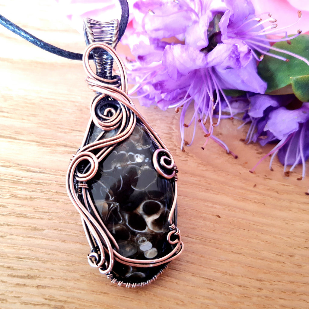 Decorative pendant with intricate wirework on a wooden surface with purple flowers in the background