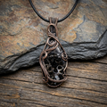 Copper wire-wrapped Turritella Agate pendant with a dark stone on a wooden surface