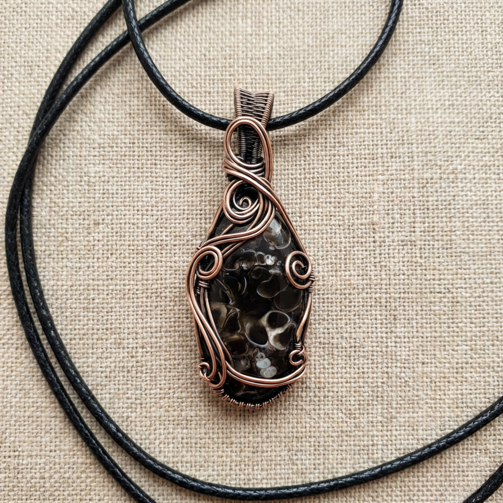 Copper-wrapped pendant with a textured stone on a black cord against a beige fabric background