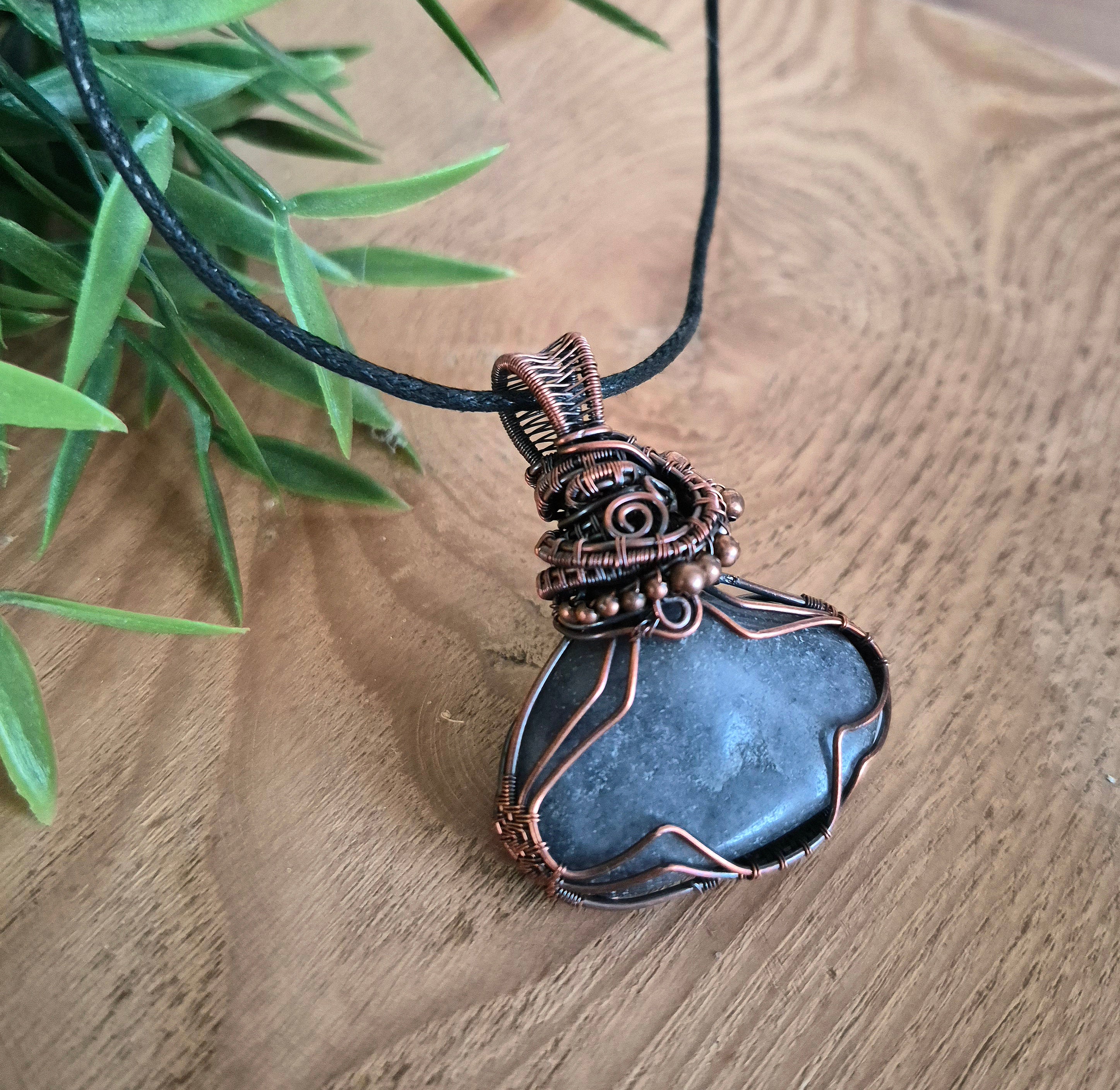 Necklace with a blue stone pendant on a wooden surface with green leaves.