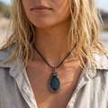 Close-up of a person wearing a necklace with a green pendant outdoors