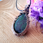 Green stone pendant with wire wrapping on a wooden surface with purple flowers